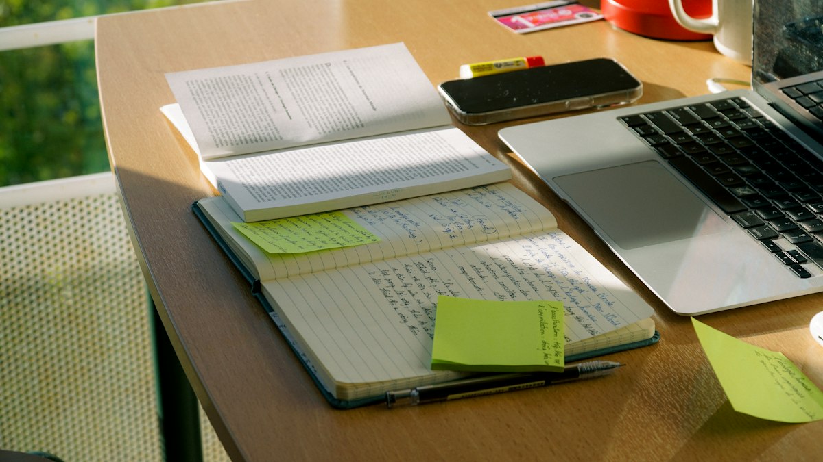 Mesa de estudio con cuaderno, libros y ordenador portátil.